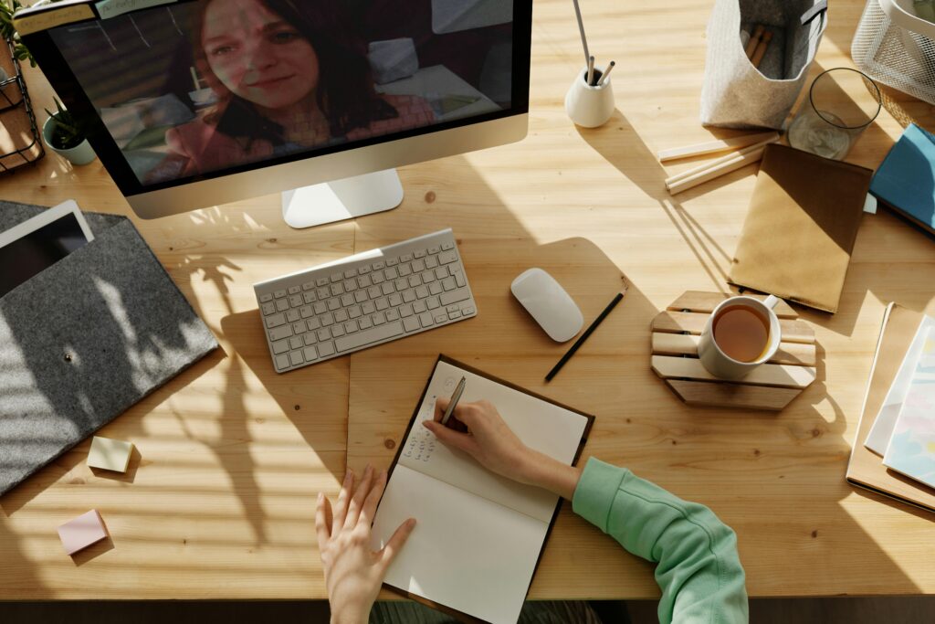 Student taking notes during an online GCSE English tutoring session, with a tutor visible on the computer screen